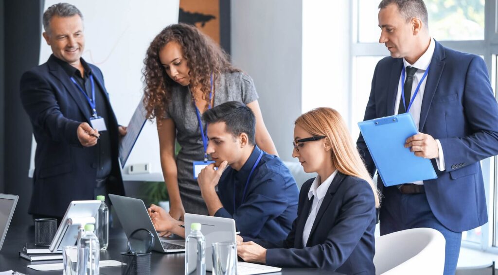 Business team collaborating in a modern conference room, reviewing work on laptops and tablets with documents and charts.
