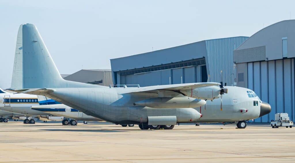 Military cargo aircraft parked on the tarmac in front of large airport hangars.